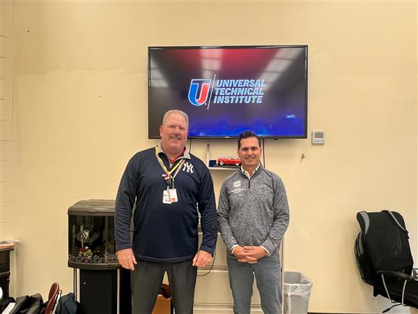 VP Mattei poses with a Universal Technical Institute Representative in front of the UTI logo. 